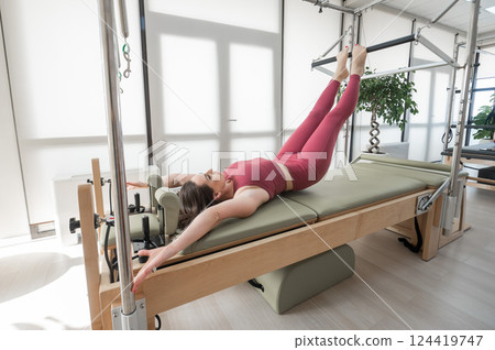 Woman doing pilates exercise on cadillac reformer machine.  124419747