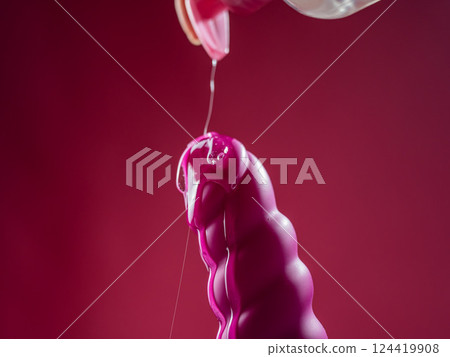 Lube pouring on pink dildo on pink background.  124419908