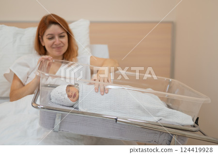 A young mother admires her newborn son in the maternity hospital.  124419928