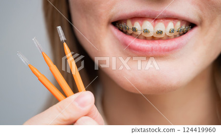 Close-up portrait of a woman with braces holding a floss to clean her teeth.  124419960