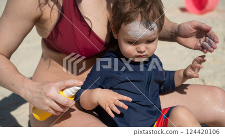 Caucasian woman applies sunscreen to her one-year-old son's skin. Caucasian woman applies sunscreen to her one-year-old son's skin. 124420106
