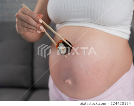 A pregnant woman holds a roll with chopsticks. Close-up of the belly. A pregnant woman holds a roll with chopsticks. Close-up of the belly. 124420154