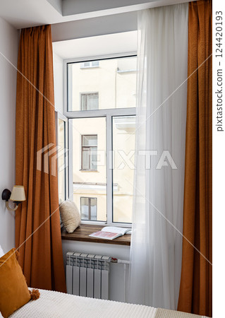 A stylish bedroom window adorned with elegant curtains and cozy decor creates a warm atmosphere A stylish bedroom window adorned with elegant curtains and cozy decor creates a warm atmosphere 124420193