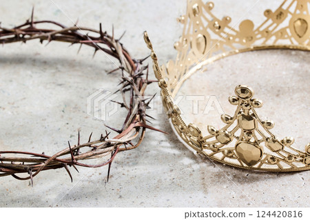 A crown of thorns lies beside an ornate golden crown 124420816