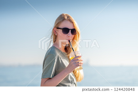 Young woman in sunglasses enjoying a refreshing drink at the beach. 124420848