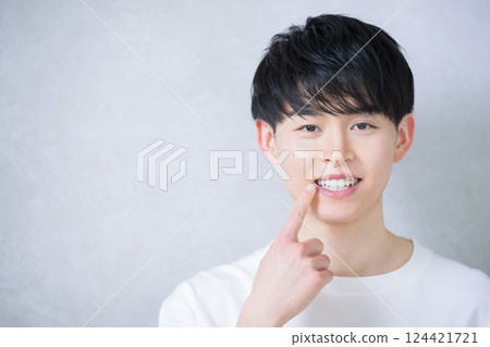 A young man in his 20s pointing at his teeth alignment. Image of whitening and orthodontics 124421721