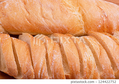 Wheat baguette sliced and whole close-up as a background. Wheat baguette sliced and whole close-up as a background. 124422752
