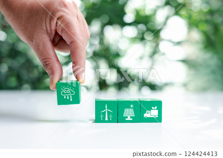 Hand put green wooden cubes with net zero icon and white icon on bokeh nature. Net zero and carbon neutral concept. Net zero greenhouse gas emissions target. Climate neutral long term strategy. 124424413