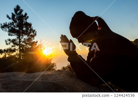 Silhouette of christian woman prayer on sunset background. Woman raising his hands in worship for peaceful life. Female praising God on the mountain. Christian religion concept. Silhouette of christian woman prayer on sunset background. Woman raising his hands in worship for peaceful life. Female praising God on the mountain. Christian religion concept. 124424536