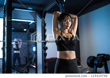 A cool woman working out at the gym stretching her shoulder blades, upper arm stretching, muscle training girl 124424740