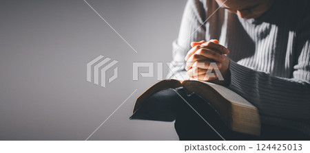 Hands folded in prayer on holy bible in church concept for faith, spirituality and religion. Unrecognizable woman holding a bible in her hands and praying. Hands clasped in prayer over holy bible. 124425013