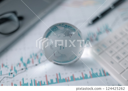 Stock market graphs and data with globe. Glass globe with stock charts, calculator and spectacles, Accounting Concept. Financial accounting stock market graphs analysis. 124425262