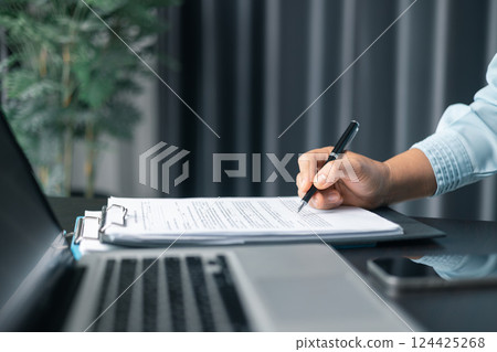 Close up businesswoman signing documents. Hand of woman write business document charts at office desk. Woman signing document, focus on female hand holding pen, putting signature at official paper. 124425268