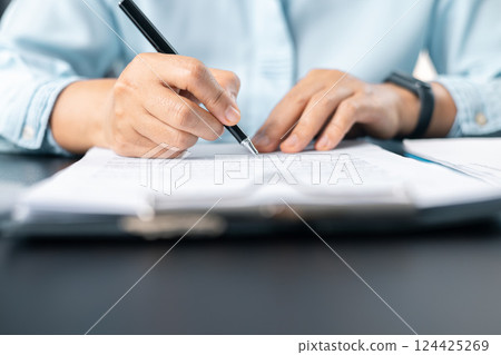 Close up businesswoman signing documents. Hand of woman write business document charts at office desk. Woman signing document, focus on female hand holding pen, putting signature at official paper. 124425269