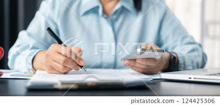 Woman signing document, focus on female hand holding pen, putting signature at official paper. Close up businesswoman signing documents. Hand of woman write business document charts at office desk. 124425306
