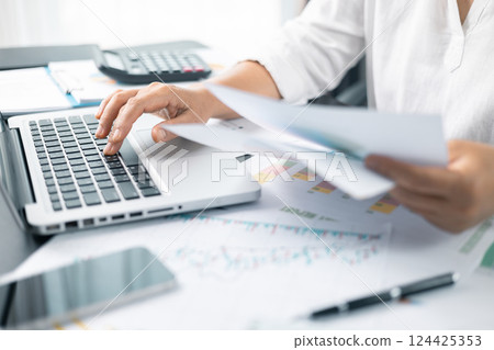 Woman analyze document in her hands. Businesswoman analyst working at office on laptop while sitting at wooden table. Business financing accounting banking concept. finance accounting. Woman analyze document in her hands. Businesswoman analyst working at office on laptop while sitting at wooden table. Business financing accounting banking concept. finance accounting. 124425353