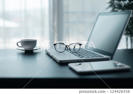 Office workplace with laptop and smart phone on wood table. Workspace, desktop computer, office supplies, houseplant and books at office. desk work concept. laptop Comfortable work table in office. 124426356