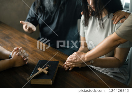 Woman gathered with her Christian friends in church, Bible close as they joined in prayer, feeling warmth of their religious family bond within group. 124426843