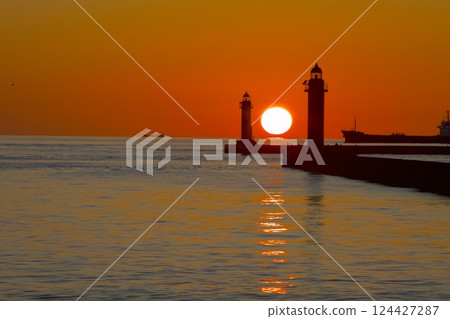 A daruma sunset sinking in the middle of the red and white lighthouse at Himeji Port 124427287