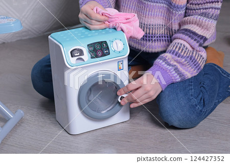 Girl play with toy iron and washing machine at home on floor. Cleaning, household chores, kids and educational games.  124427352