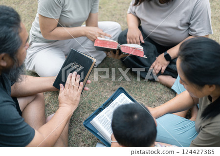 Young woman held her mother's hand in prayer, surrounded by their outdoor community, where love and family life flourished through shared moments of prayer and support. Group christian pray concept. 124427385