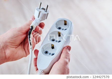 Charred extension cord with tee after being overloaded by powerful heating appliance. 124427570