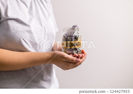 Woman holding coins and cash in jar with words Give or Donate elegantly lettered on its front, embodying spirit of giving. words, lettering, donate, jar, money, giving, woman, give, coin. 124427955
