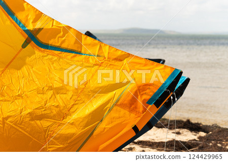 Close up detail of one bright orange kite surfer, wing kite equipment lies on sand on bright sunny day. Active sports travel concept Close up detail of one bright orange kite surfer, wing kite equipment lies on sand on bright sunny day. Active sports travel concept 124429965
