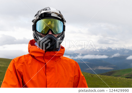 Modern motorcycle helmet with goggles on young guy standing in field with foggy mountains in background, portrait Modern motorcycle helmet with goggles on young guy standing in field with foggy mountains in background, portrait 124429990