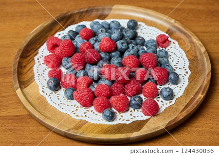 A plate of fresh berries sits on a wooden surface, enhanced by a lace doily, perfect for breakfast 124430036