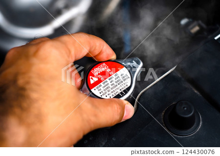 Hand removing the radiator cap from a car radiator while the radiator coolant overheated Hand removing the radiator cap from a car radiator while the radiator coolant overheated 124430076