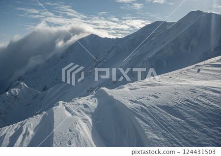 Snow smoke falling on the mountainside; steep ridges of snowy mountains; climbing snowy mountains in March Snow smoke falling on the mountainside; steep ridges of snowy mountains; climbing snowy mountains in March 124431503