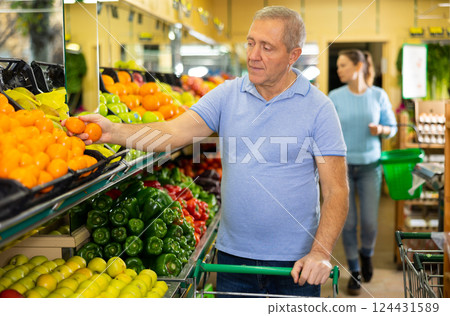 Elderly male pensioner in casual wear choosing tangerines in supermarket Elderly male pensioner in casual wear choosing tangerines in supermarket 124431589