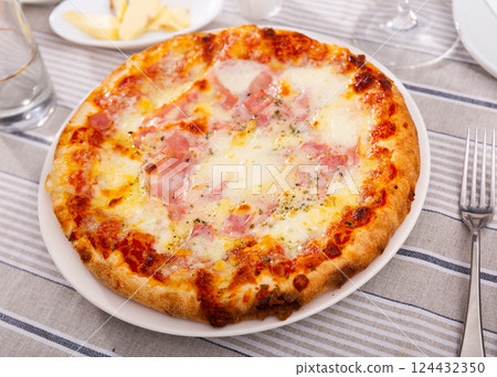 On plate is large round pizza with dried prosciutto bacon and topped with melted cheese On plate is large round pizza with dried prosciutto bacon and topped with melted cheese 124432350