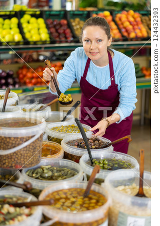 Middle-aged saleswoman showing olives in grocery store 124432393