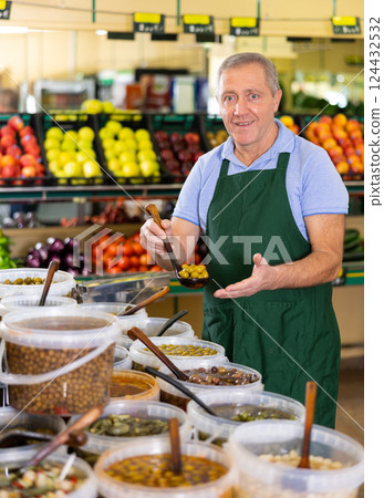 Elderly salesman showing olives in grocery store Elderly salesman showing olives in grocery store 124432532