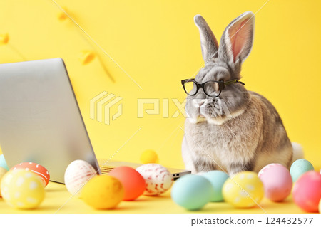 Cheerful easter bunny with glasses at laptop surrounded by colorful eggs 124432577
