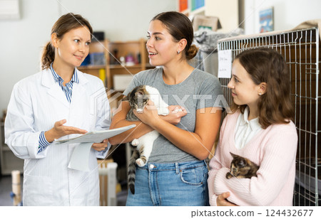 Female worker of animal shelter talking to girls adopting cats 124432677