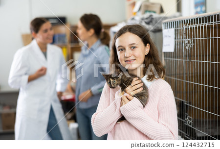 Tween girl standing in animal shelter with little kitten 124432715