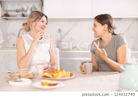 Girlfriends laugh and talk at table with tea and treats 124432740