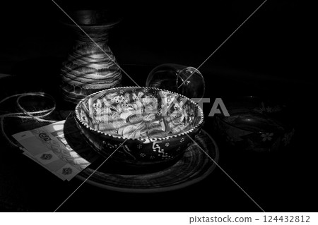 Jug and coins from different countries in a bowl with oriental patterns in a ray of light in dark 124432812