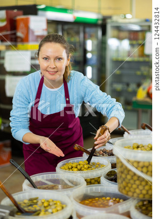 Middle-aged saleswoman showing olives in grocery store Middle-aged saleswoman showing olives in grocery store 124432814