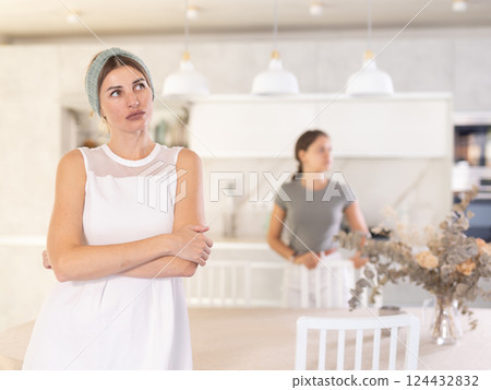 Offended mother standing in the kitchen with her back to upset young daughter Offended mother standing in the kitchen with her back to upset young daughter 124432832