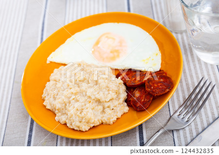 Homemade hearty breakfast - boiled oatmeal, fried eggs with chorizo sausage. Spanish dish Homemade hearty breakfast - boiled oatmeal, fried eggs with chorizo sausage. Spanish dish 124432835