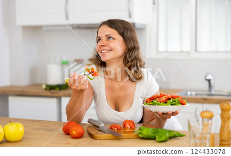 Young woman eating vegetable salad in kitchen 124433078