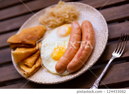 Fried sausages with scrambled eggs, pancakes and cabbage on a wooden background Fried sausages with scrambled eggs, pancakes and cabbage on a wooden background 124433082