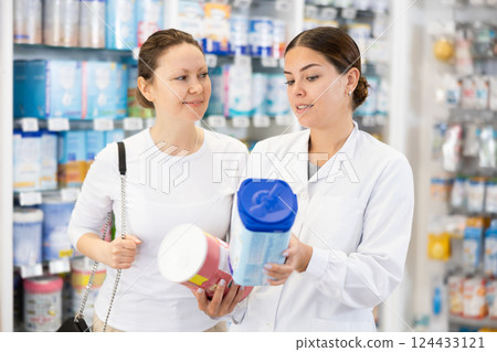Woman pharmacist helping woman customer choose baby formula in pharmacy Woman pharmacist helping woman customer choose baby formula in pharmacy 124433121