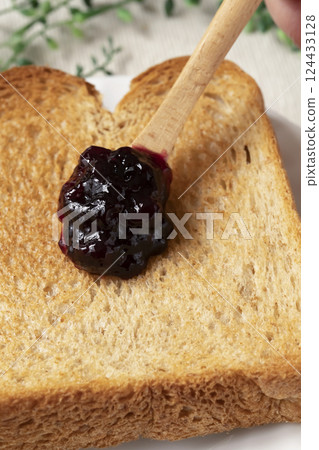 Spread bottled blueberry jam onto toasted bread Spread bottled blueberry jam onto toasted bread 124433128