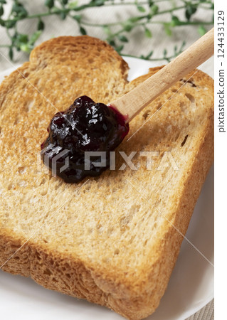 Spread bottled blueberry jam onto toasted bread Spread bottled blueberry jam onto toasted bread 124433129