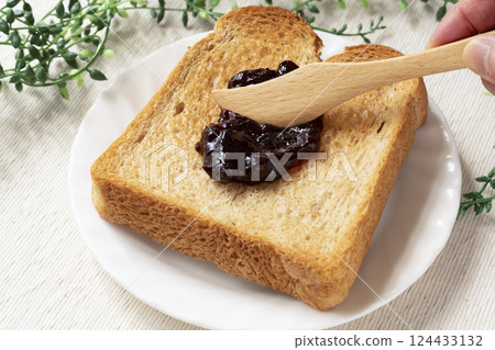 Spread bottled blueberry jam onto toasted bread Spread bottled blueberry jam onto toasted bread 124433132